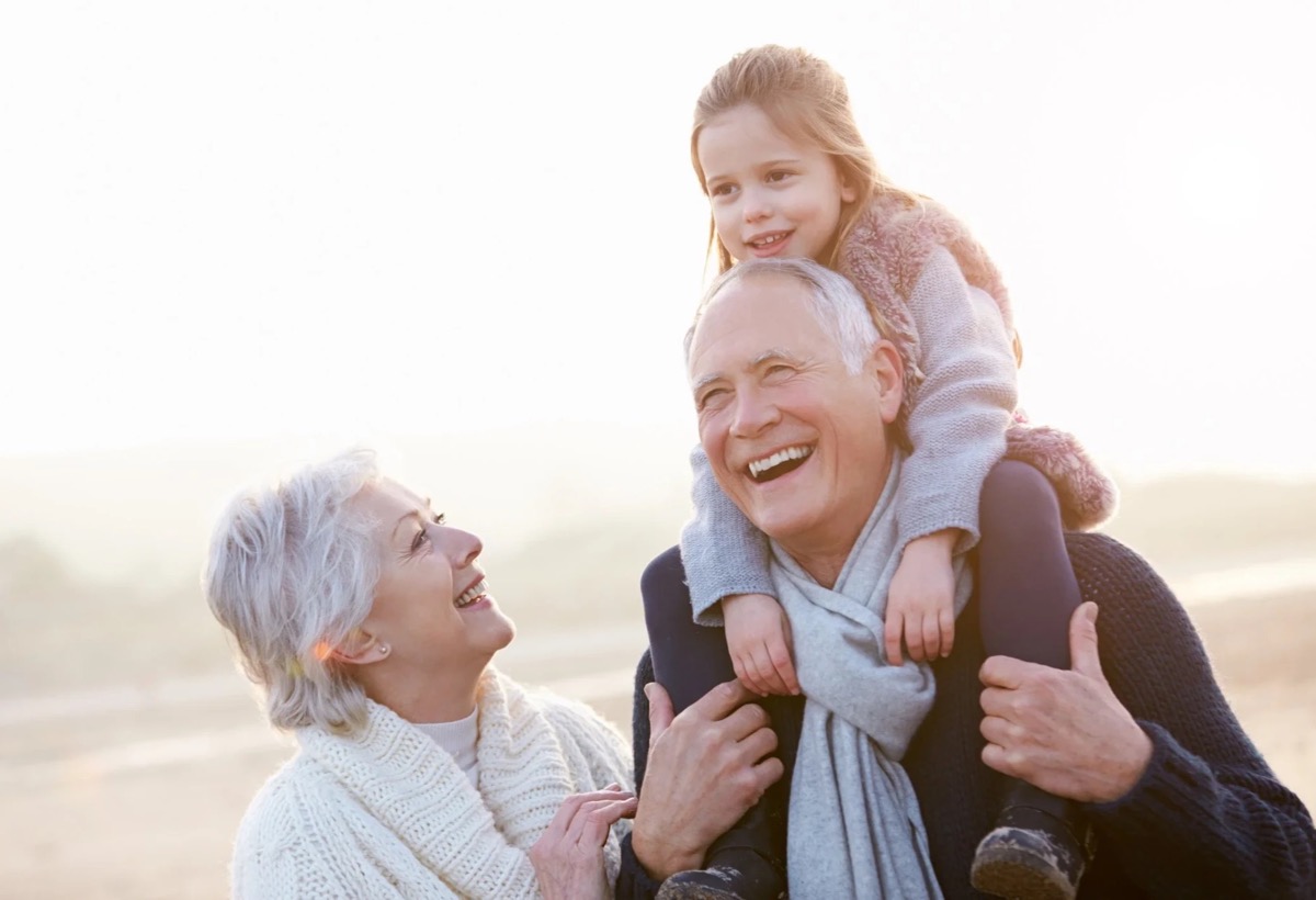 Grandparents laughing with their granddaughter on her grandfather's shoulders